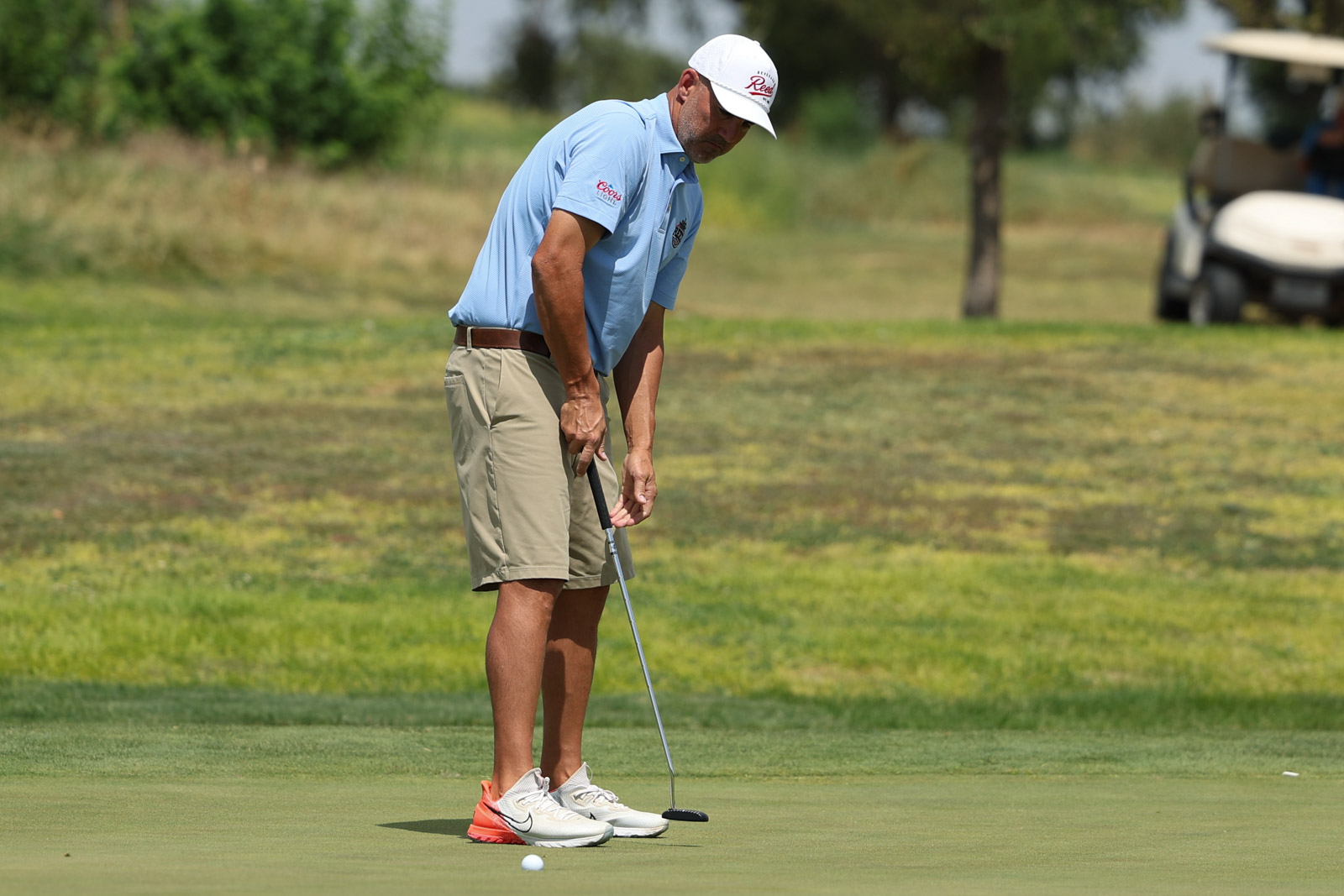 CoorTOC_FinalDay-56 | Press Pass Sports Golfer preparing to putt on a green, wearing a light blue polo and beige shorts with a white cap.