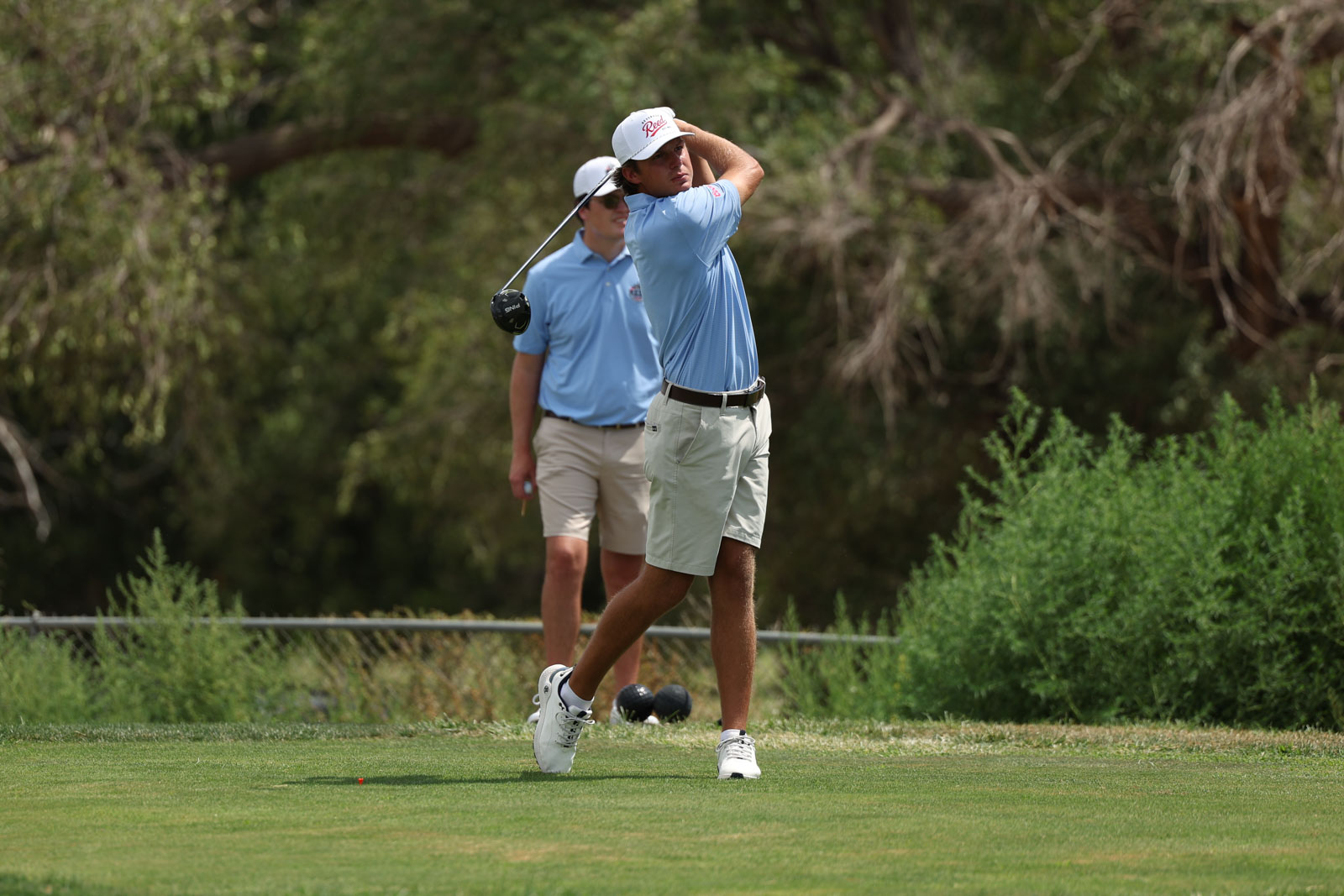 CoorTOC_FinalDay-57 | Press Pass Sports Golfer in light blue polo and white cap watches his tee shot on a sunny golf course, with caddie in background.