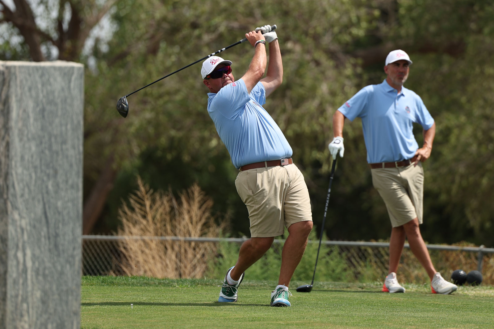 CoorTOC_FinalDay-59 | Press Pass Sports Golfer in a light blue shirt and beige shorts mid-swing with a driver on a sunny golf course, another player watching in the background.
