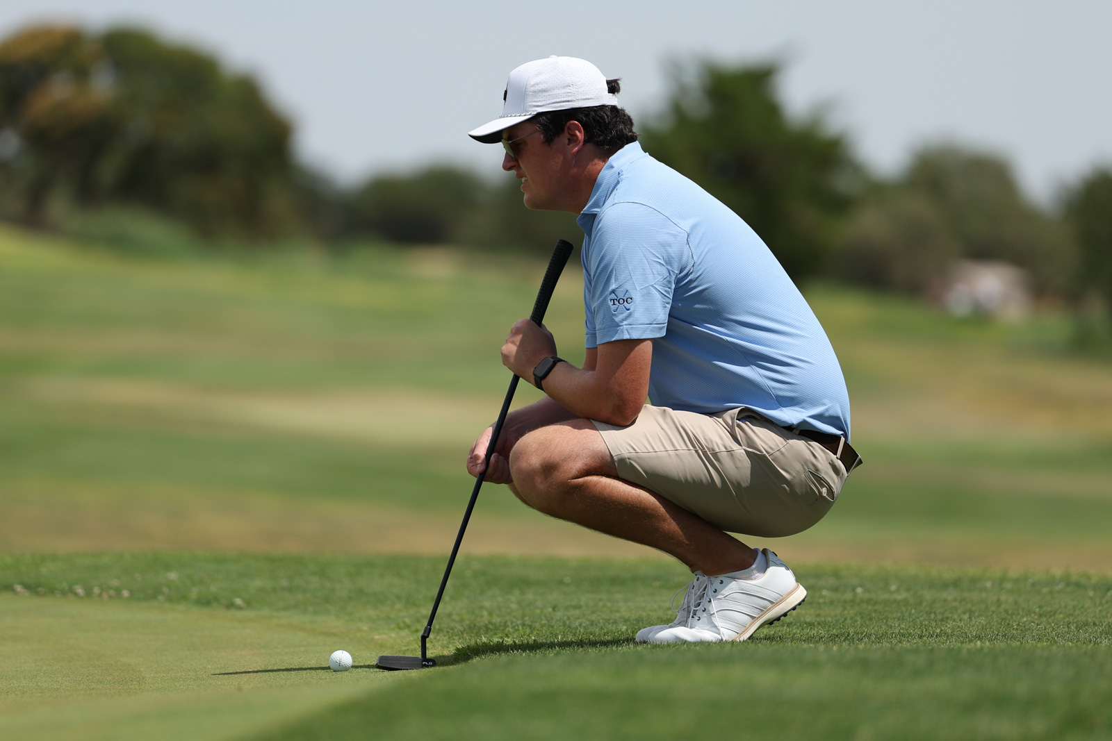 CoorTOC_FinalDay-62 | Press Pass Sports Golfer crouched on the putting green, lining up a putt with a black putter.
