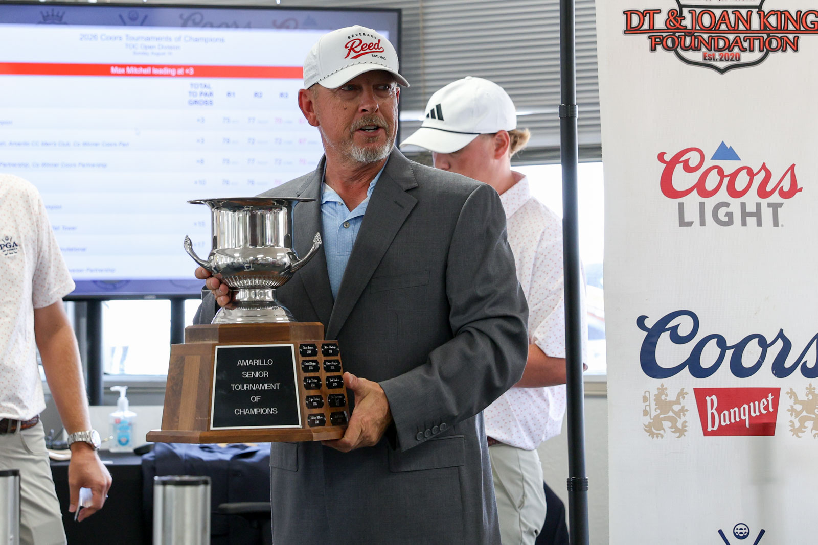 CoorTOC_FinalDay-70 | Press Pass Sports Man in a gray suit holding a large silver trophy at an awards ceremony, plaque reads Amarillo Senior Tournament of Champions.