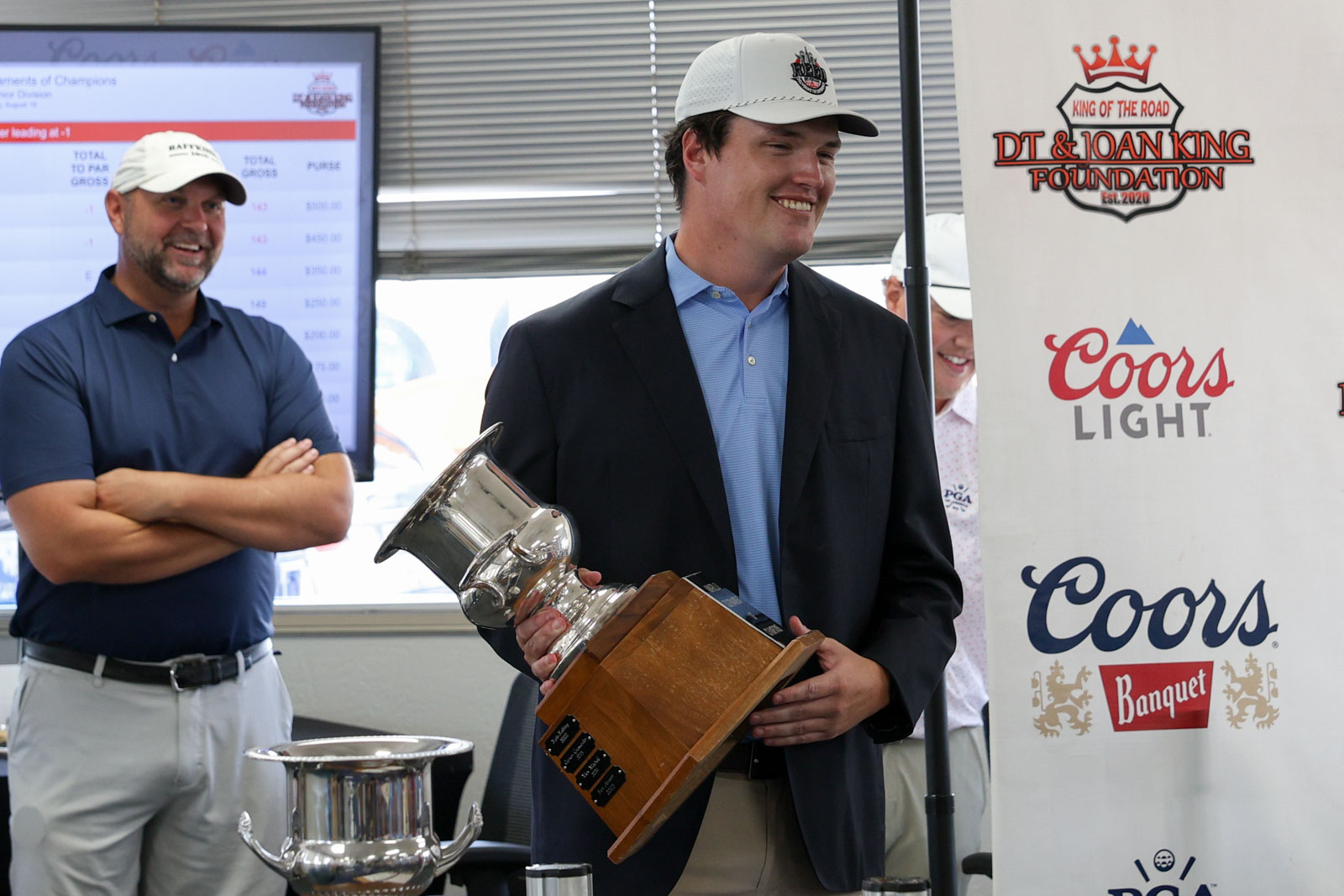 CoorTOC_FinalDay-73 | Press Pass Sports Man in a blazer and light blue polo holds a large trophy with a wooden base at an awards ceremony.