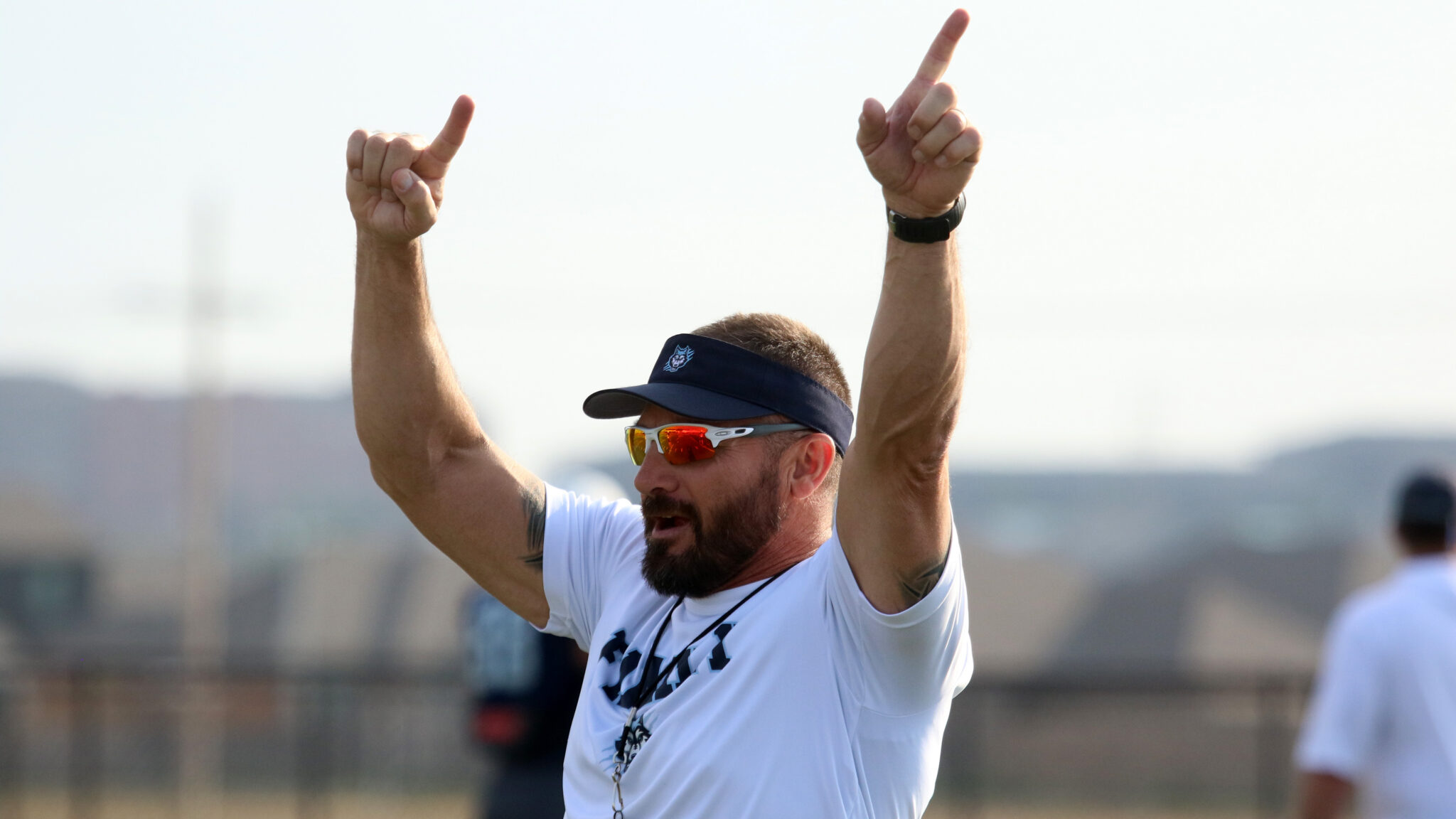 West Plains - HC Jeff Lofton 2 1 | Press Pass Sports Bearded man in sunglasses and a navy visor raises both arms in celebration outdoors, thumbs up.
