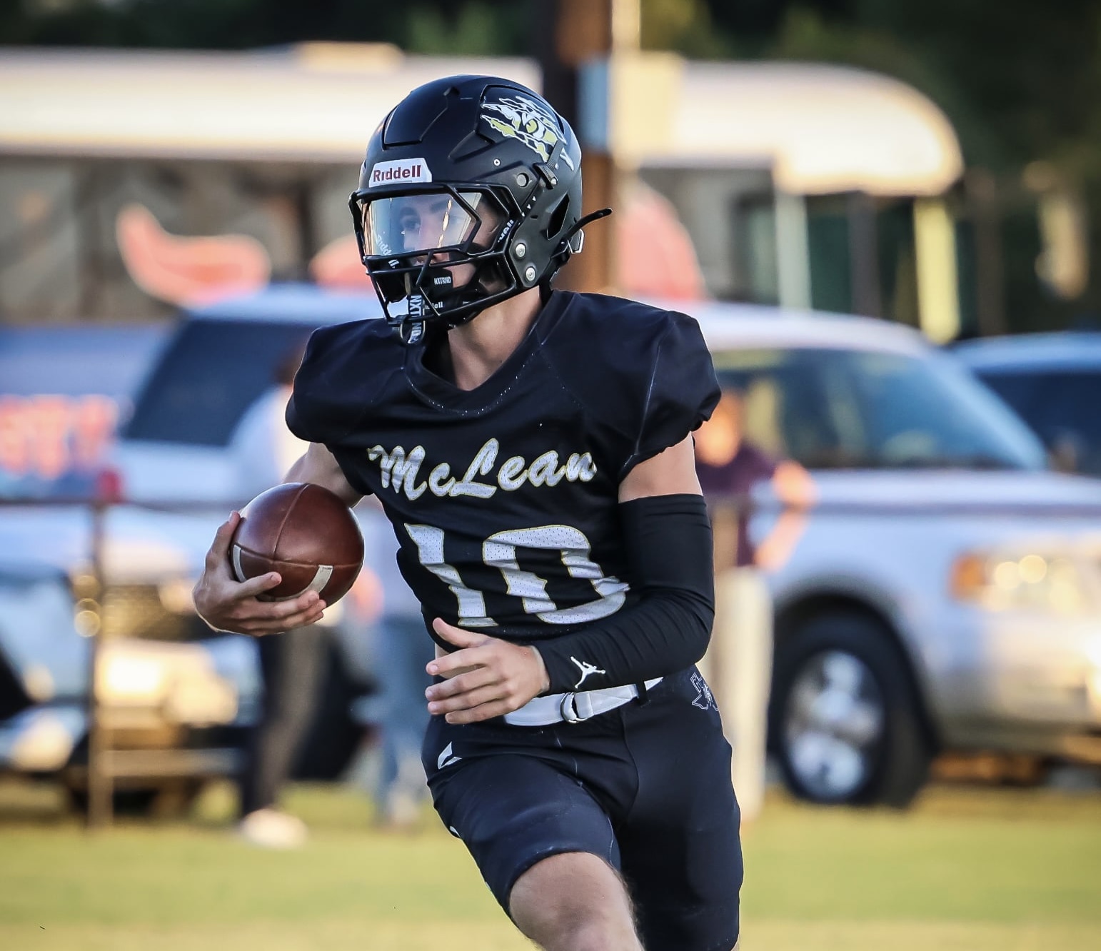 Youth football player in a black McLean jersey with number 10 runs with the ball on a grassy field.