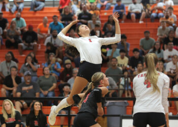 20260818-Tascosa-Caprock-VB-005 | Press Pass Sports Female volleyball player in a white jersey number 1 leaps upward to spike, with a crowded orange gym audience in the background.