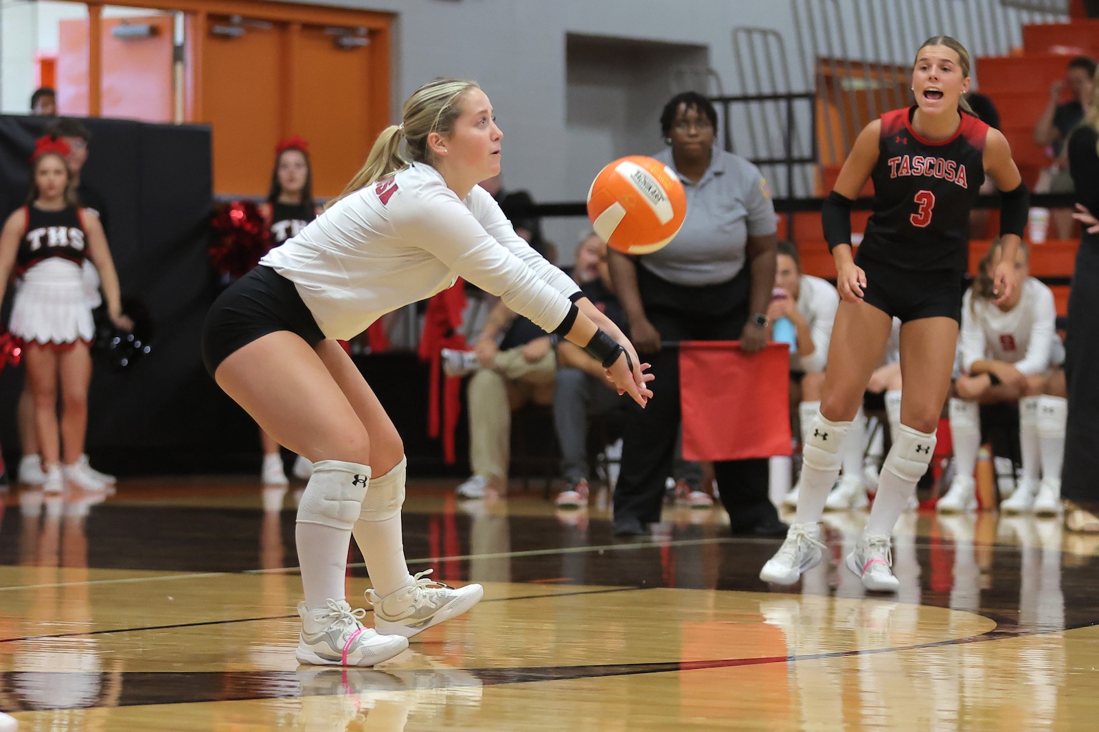 Female volleyball player in white dives to pass an approaching orange ball, with a Tascosa teammate in black and red nearby.