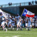 MY4A4954 | Press Pass Sports Spearman football players in white uniforms run onto the field carrying flags (Texas, USA) as fans watch from the stands above the tunnel area.