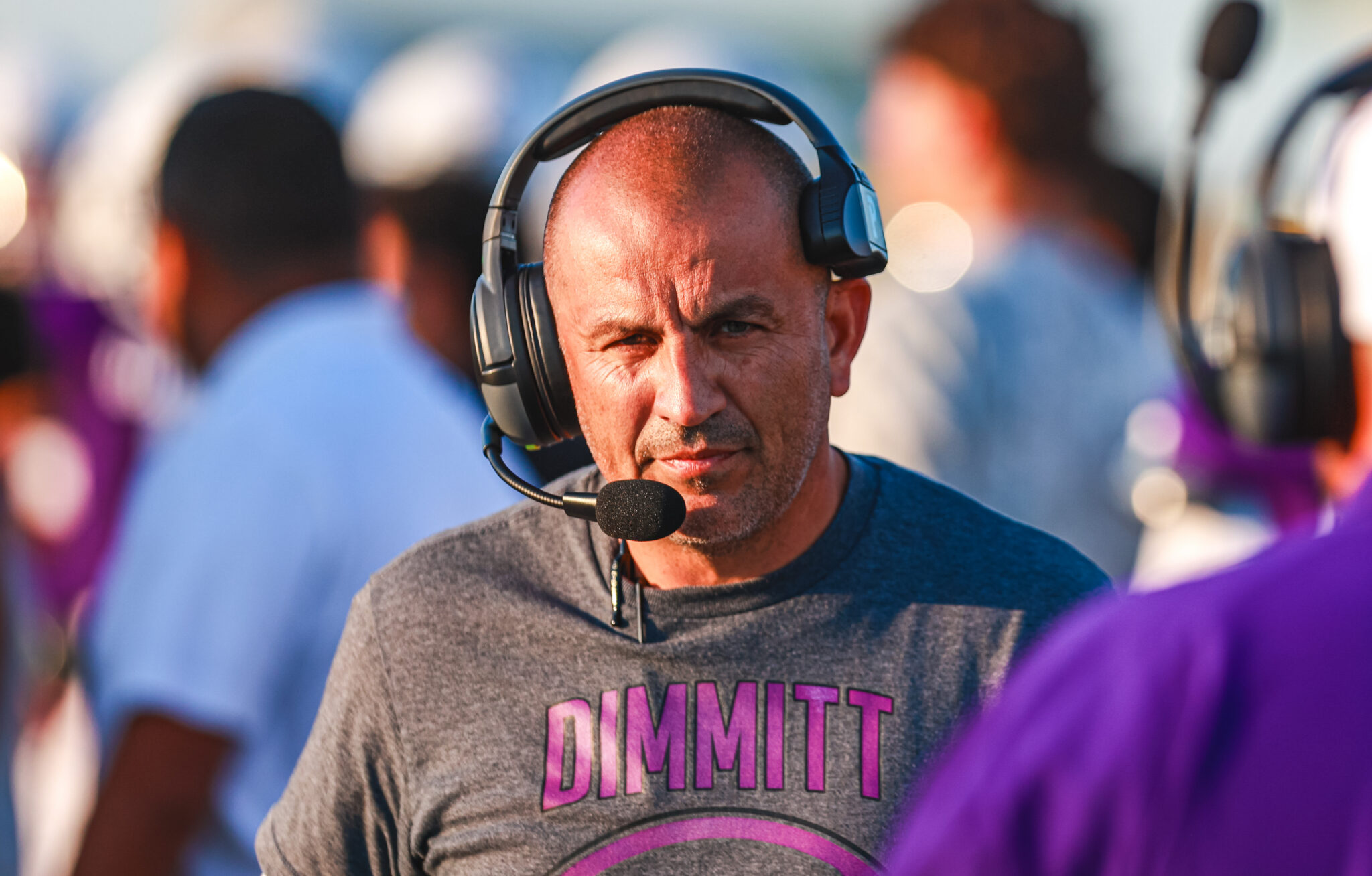 1H4A6168 | Press Pass Sports Man wearing a large over-ear headset with microphone, looking toward the camera at a busy event venue.