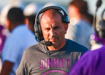 1H4A6168 | Press Pass Sports Man wearing a large over-ear headset with microphone, looking toward the camera at a busy event venue.