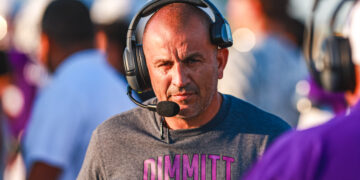 Man wearing a large over-ear headset with microphone, looking toward the camera at a busy event venue.