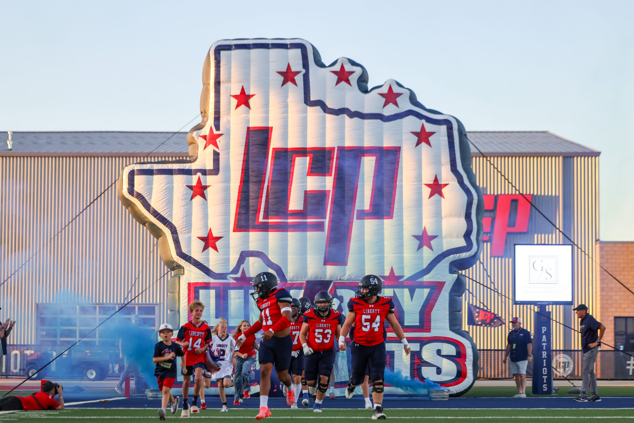 Seabolt Chase-2745 | Press Pass Sports Football players in red uniforms run onto the field from a large star-shaped inflatable tunnel.