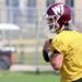 1K6A6710 | Press Pass Sports Football player in a yellow practice jersey holding a ball, wearing a maroon helmet on a sunny field.