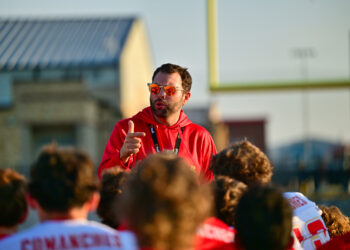 DSC_8691 | Press Pass Sports Man in a red hoodie with orange sunglasses addressing a crowd outdoors at a sports event.