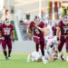 West Texas A&M quarterback #9 runs with the ball as teammates block near a sunny football field.