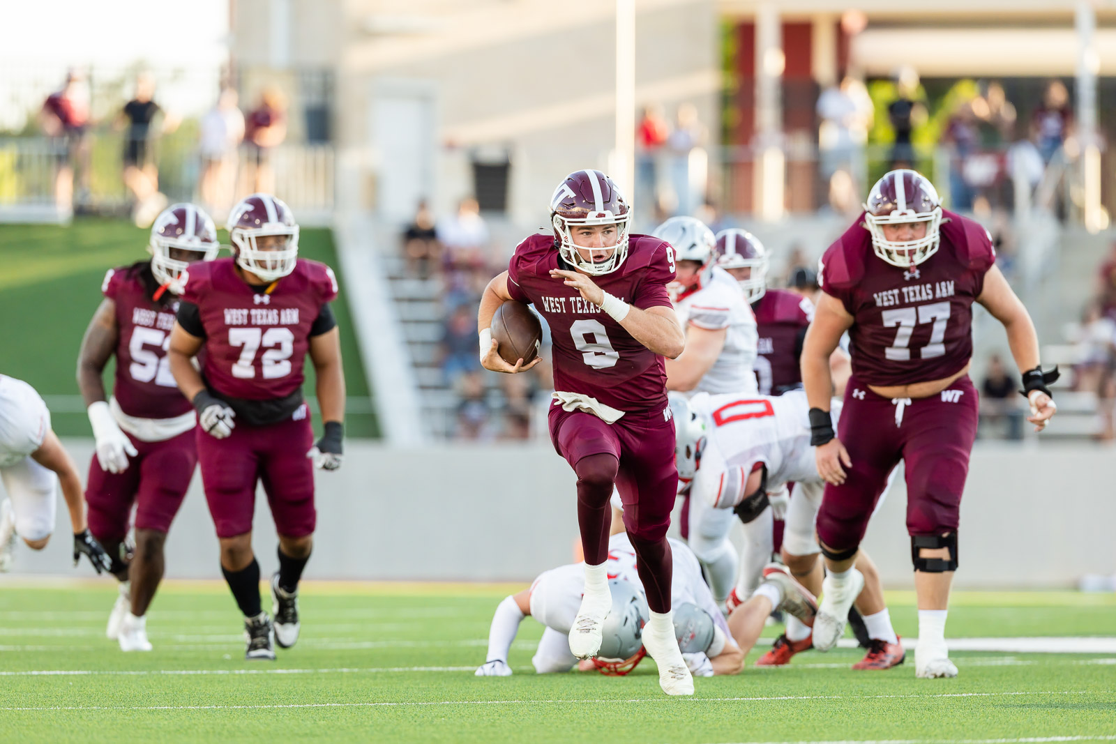 western-colorado-vs-wtamu-jpegJoe-pps-12 | Press Pass Sports West Texas A&M quarterback #9 runs with the ball as teammates block near a sunny football field.