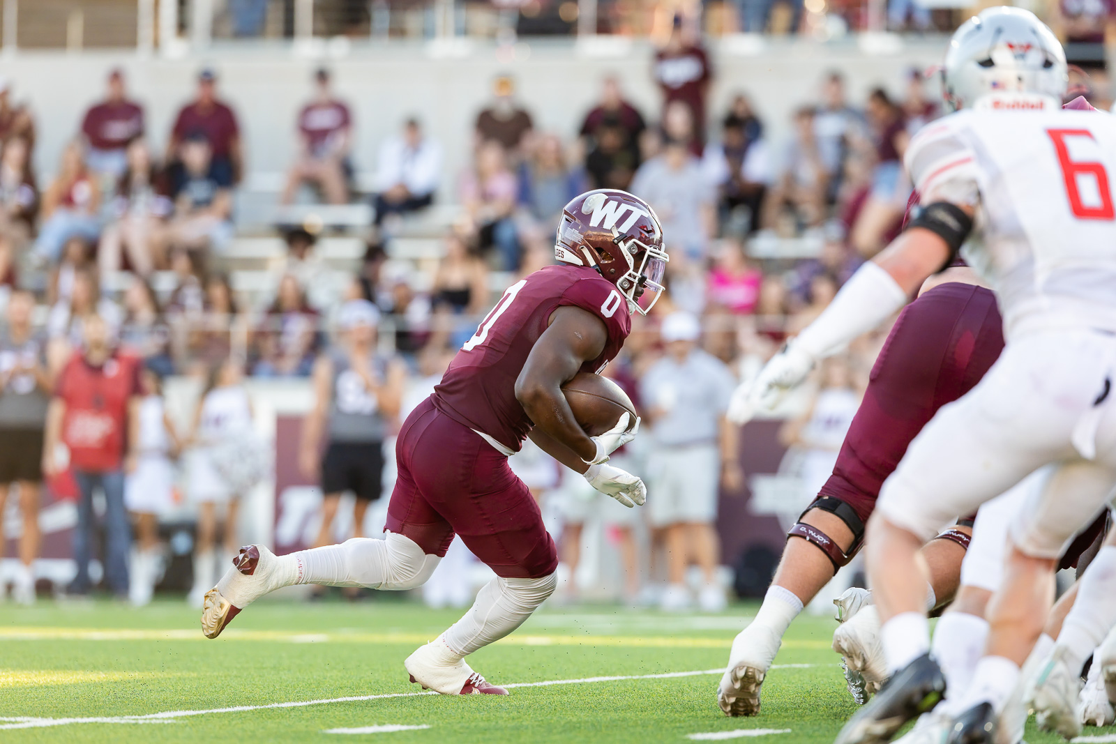 western-colorado-vs-wtamu-jpegJoe-pps-20 | Press Pass Sports Football player in maroon uniform runs with the ball, sprinting past defenders on a green field with a cheering crowd in the stands.