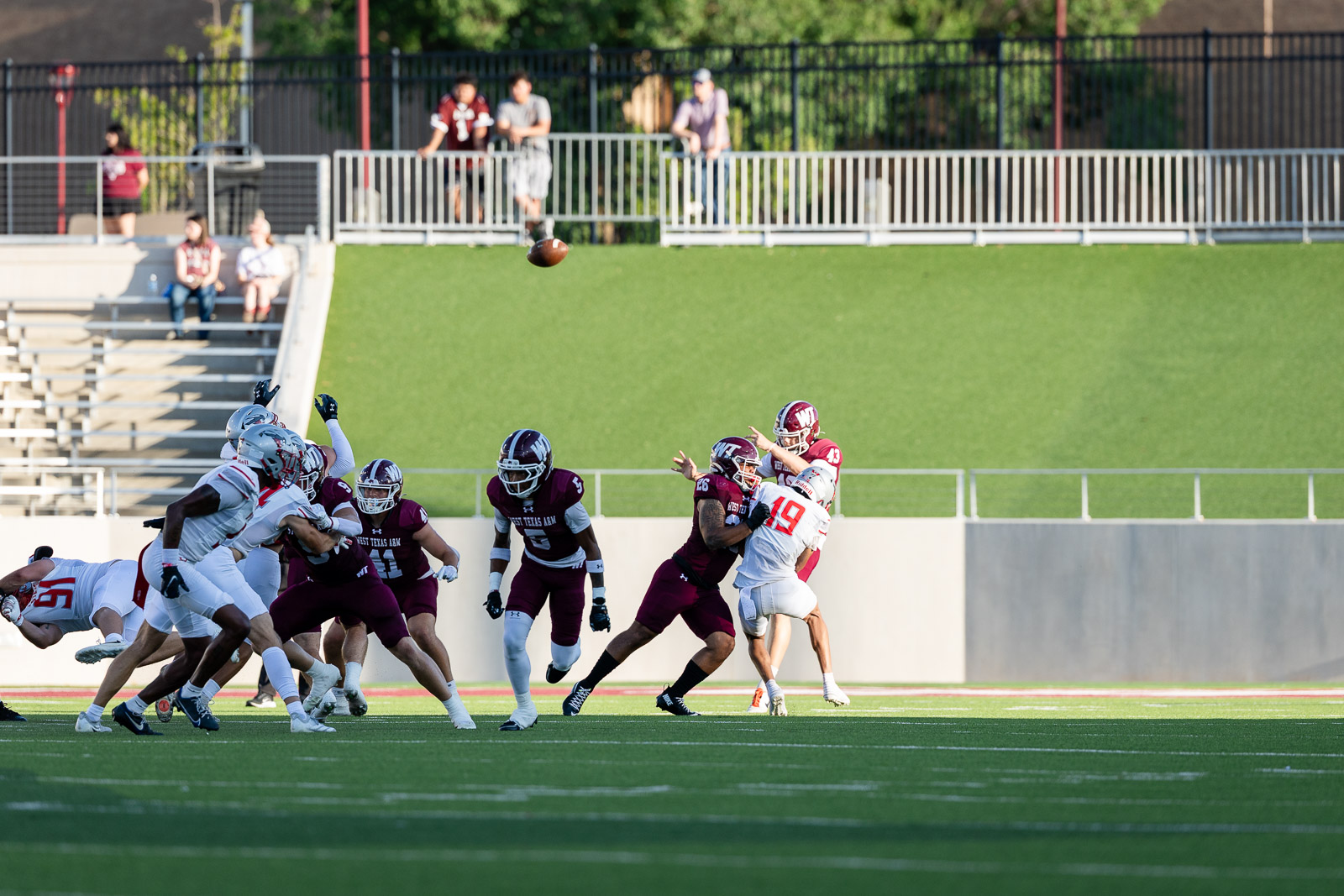 western-colorado-vs-wtamu-jpegJoe-pps-6 | Press Pass Sports Football game scene: quarterback in white (#19) is tackled as the ball sails through the air, maroon-clad defenders converging nearby on a sunny field.