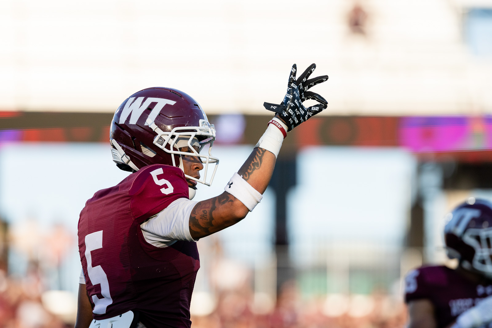 western-colorado-vs-wtamu-jpegJoe-pps-8 | Press Pass Sports Football player in a maroon jersey (number 5) and white gloves raises his gloved hand in celebration on the field, helmet with WT logo visible.