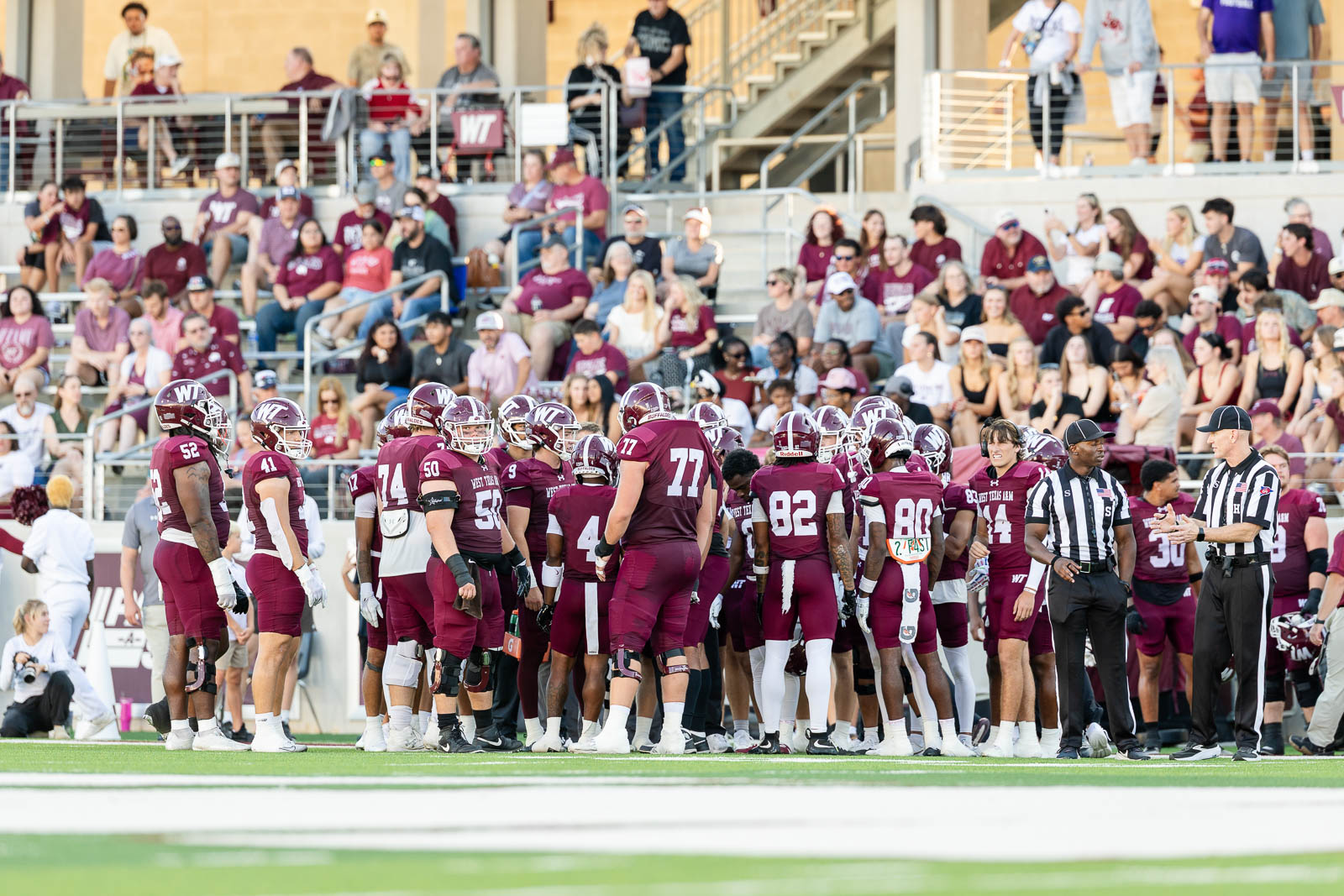 western-colorado-vs-wtamu-jpegJoe-pps-9 | Press Pass Sports College football team in maroon uniforms huddles on the field while spectators watch from the stands behind them.