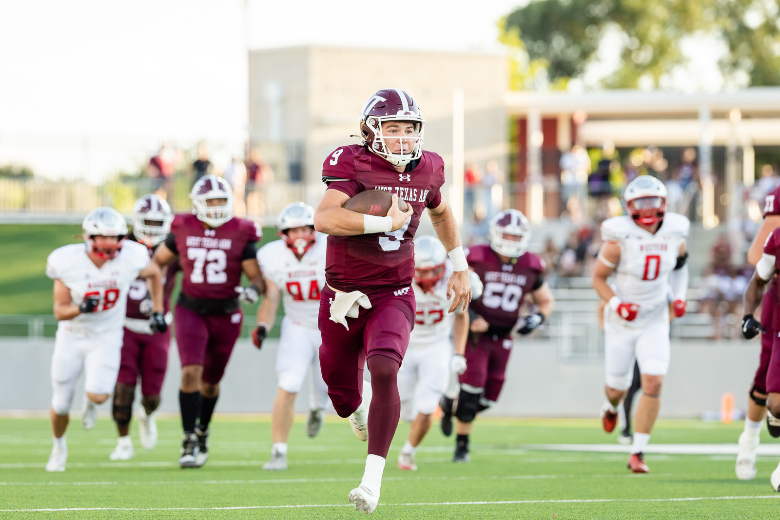 western-colorado-vs-wtamu-jpegJoe-pps-13 | Press Pass Sports Maroon-clad quarterback runs with the ball during a high school football game on a green field.