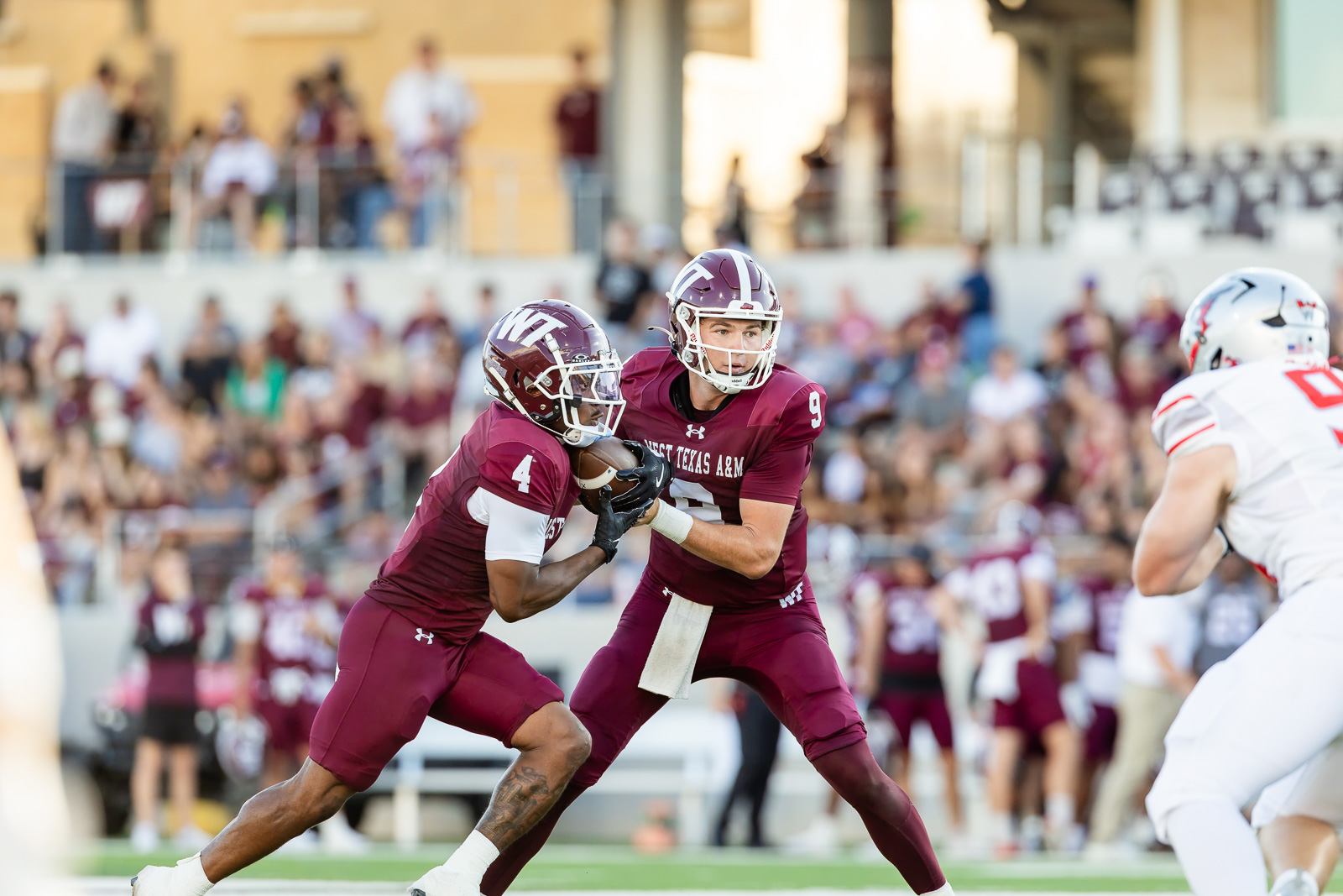 western-colorado-vs-wtamu-jpegJoe-pps-14 | Press Pass Sports Two college football players in maroon uniforms collide for the ball during a game as a defender closes in, with a crowd watching in the stands behind them