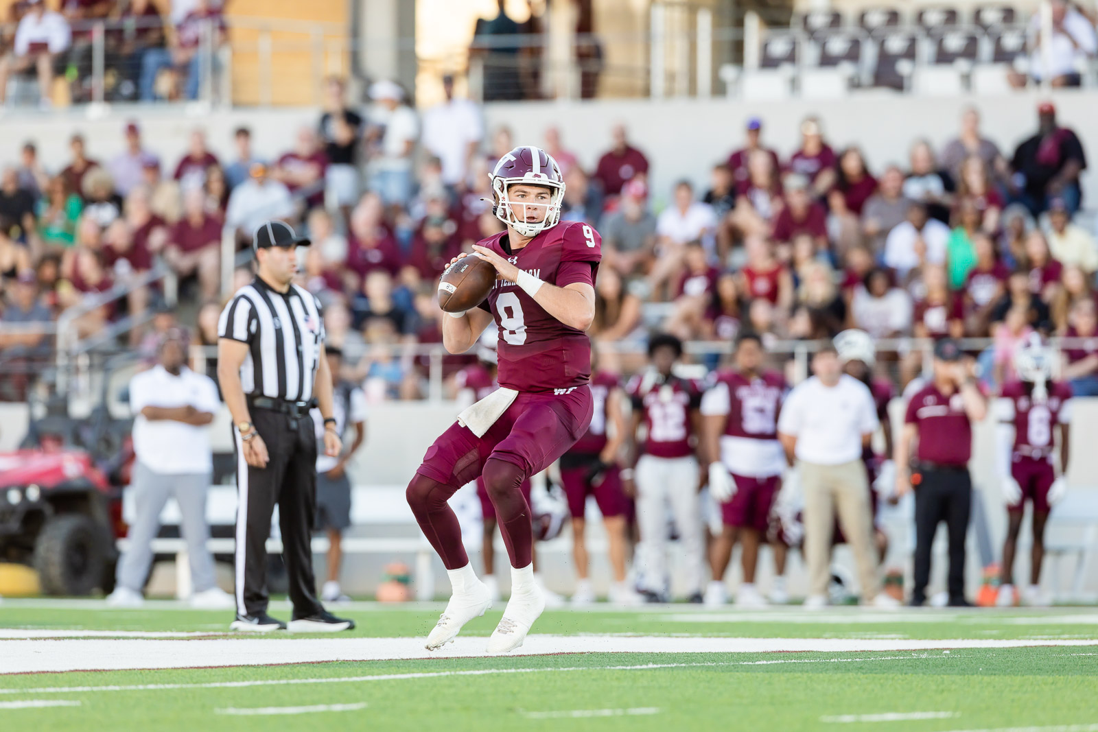western-colorado-vs-wtamu-jpegJoe-pps-15 | Press Pass Sports Quarterback in maroon #9 throwing a pass on a football field with a cheering crowd in the stands behind him.