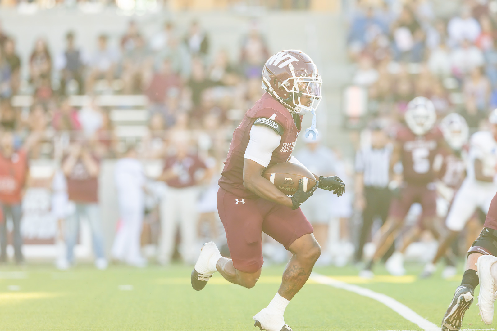 western-colorado-vs-wtamu-jpegJoe-pps-18 | Press Pass Sports Football player in maroon uniform runs with the ball during a game, crowd blurred in the stands behind him.