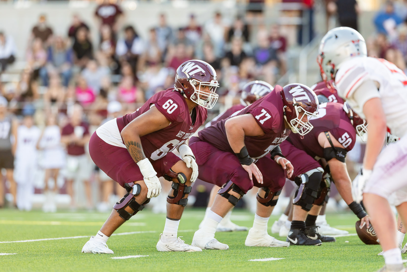 western-colorado-vs-wtamu-jpegJoe-pps-21 | Press Pass Sports Maroon-clad college football linemen crouch at the line of scrimmage on a green field, with a crowded stands backdrop behind them.