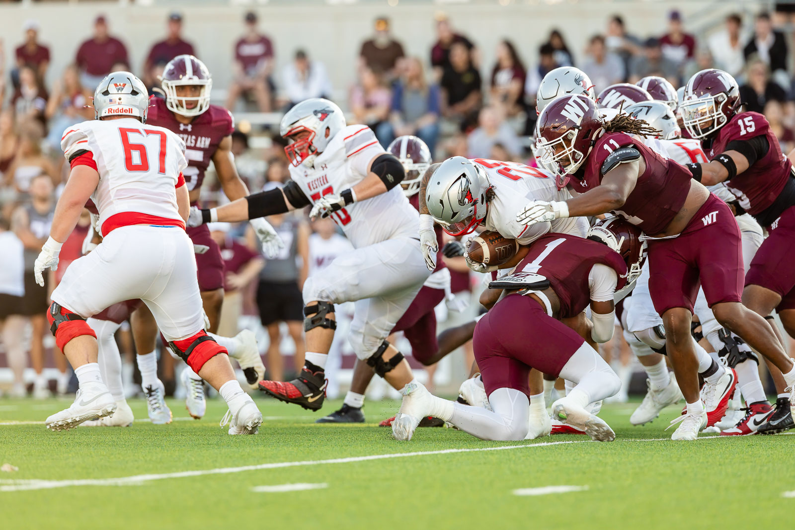 western-colorado-vs-wtamu-jpegJoe-pps-25 | Press Pass Sports Football game in progress: a ball carrier is tackled by maroon-clad defenders as white-team players converge on the pile on a bright green field.
