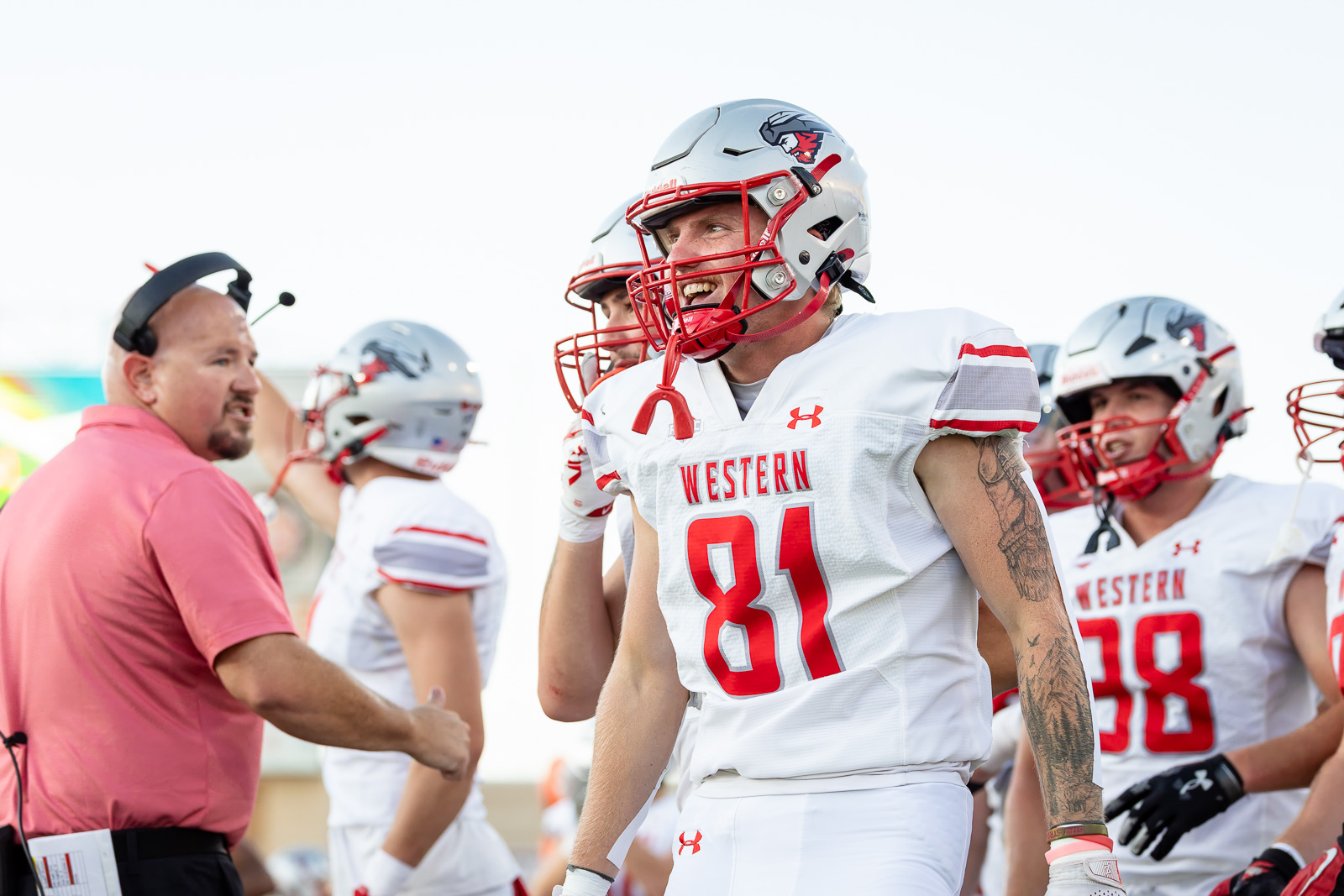 western-colorado-vs-wtamu-jpegJoe-pps-29 | Press Pass Sports Western football players in white uniforms with red numbers walk onto the field; foreground player #81 smiles in a red helmet.