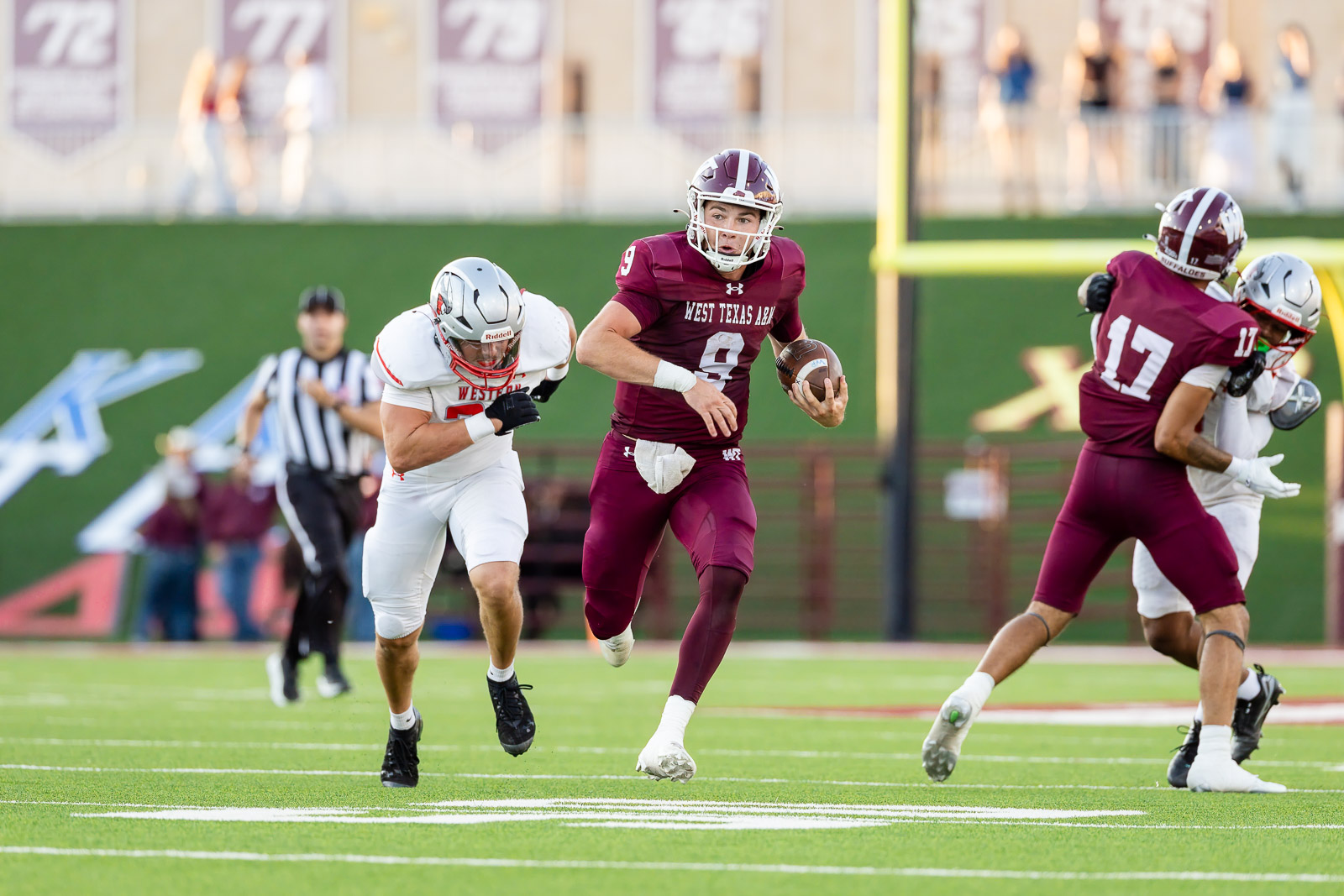 western-colorado-vs-wtamu-jpegJoe-pps-35 | Press Pass Sports American football player in maroon West Texas A&M jersey runs with the ball while tackled by opponents on a green turf field.