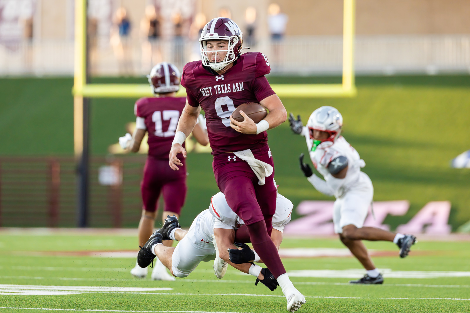western-colorado-vs-wtamu-jpegJoe-pps-36 | Press Pass Sports Maroon-clad football player runs with the ball during a game on a green field, opponents in white pursuing behind far goalpost in background