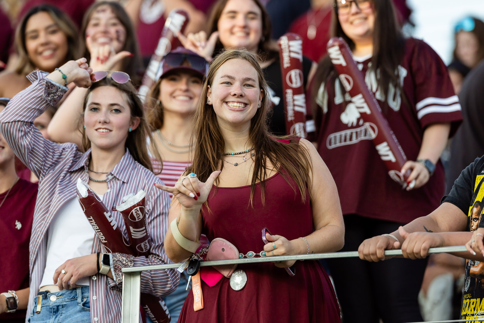 western-colorado-vs-wtamu-jpegJoe-pps-40 | Press Pass Sports Group of college fans cheering at a game, central smiling woman in a maroon dress stands at the railing.