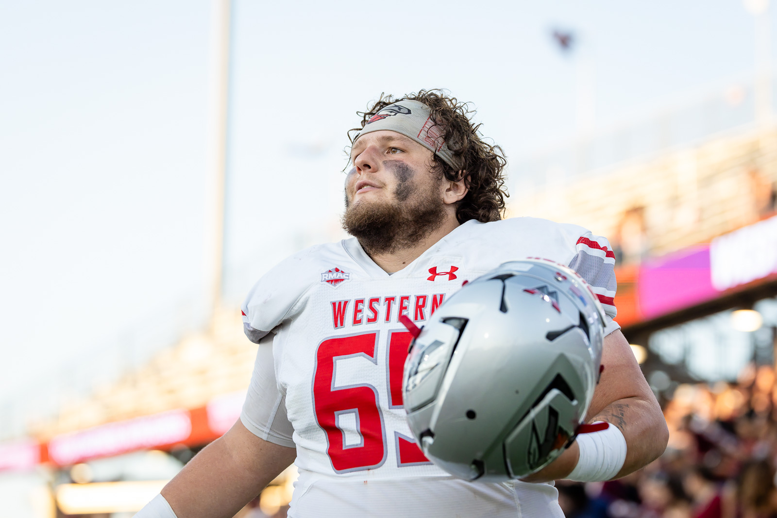 western-colorado-vs-wtamu-jpegJoe-pps-42 | Press Pass Sports A college football player in a white uniform with red accents holds a silver helmet, standing on the field with a crowd in the stands behind him.