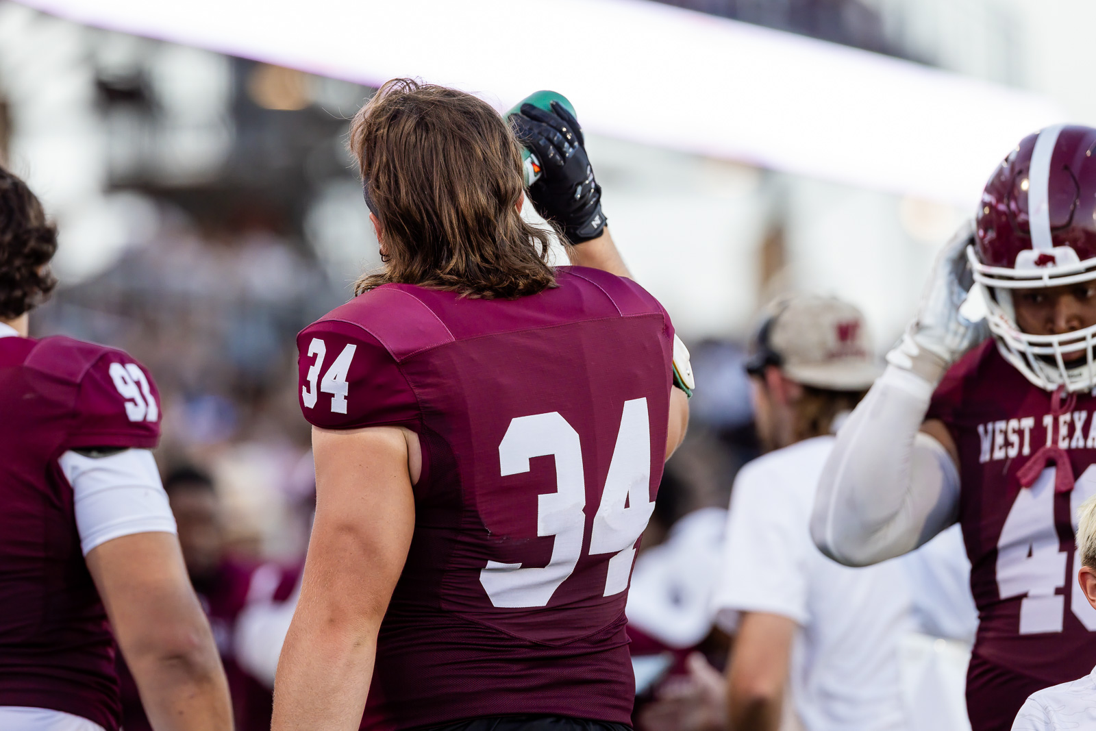 western-colorado-vs-wtamu-jpegJoe-pps-45 | Press Pass Sports Back view of football players in maroon uniforms celebrating on the sidelines, #34 prominent on center player's jersey