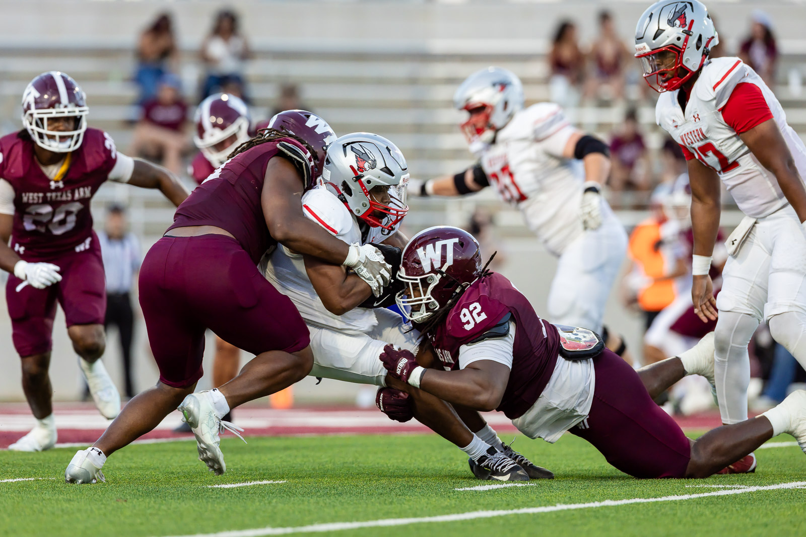 western-colorado-vs-wtamu-jpegJoe-pps-48 | Press Pass Sports Maroon-clad defenders tackle a white-jersey ball carrier during a college football play on a green field.