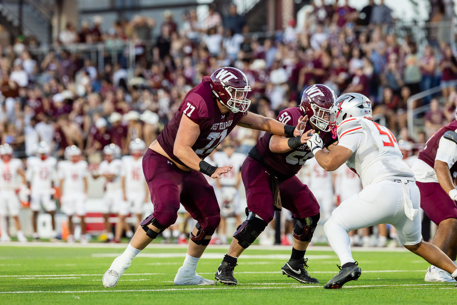 western-colorado-vs-wtamu-jpegJoe-pps-55 | Press Pass Sports Maroon-uniformed football players tackle a white-uniform opponent on a bright green field with a packed crowd in the background.
