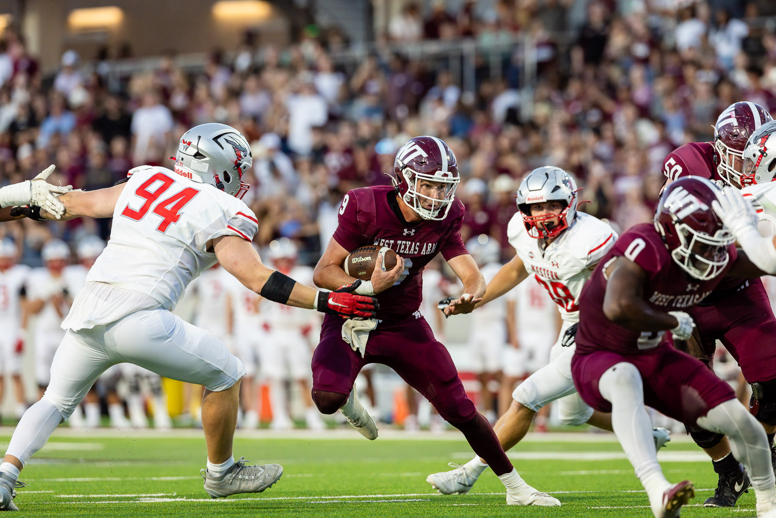western-colorado-vs-wtamu-jpegJoe-pps-56 | Press Pass Sports A West Texas A&M player in maroon runs with the football as a defender closes in during a college football game with a crowded stadium in the background.