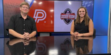 Two news anchors stand at a desk in a studio, a large screen behind them shows the red 'P' logo and a 'The Locker Room' graphic for Fox 14.