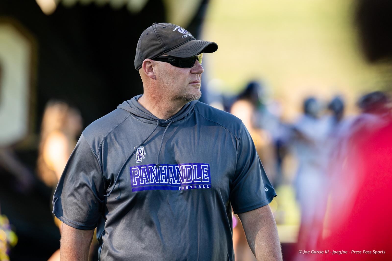 panhnandle-vs-canadian-football-jpegJoe-pps-1 | Press Pass Sports Side-profile man wearing a gray Panhandle Football shirt and cap, with sunglasses, at an outdoor event.