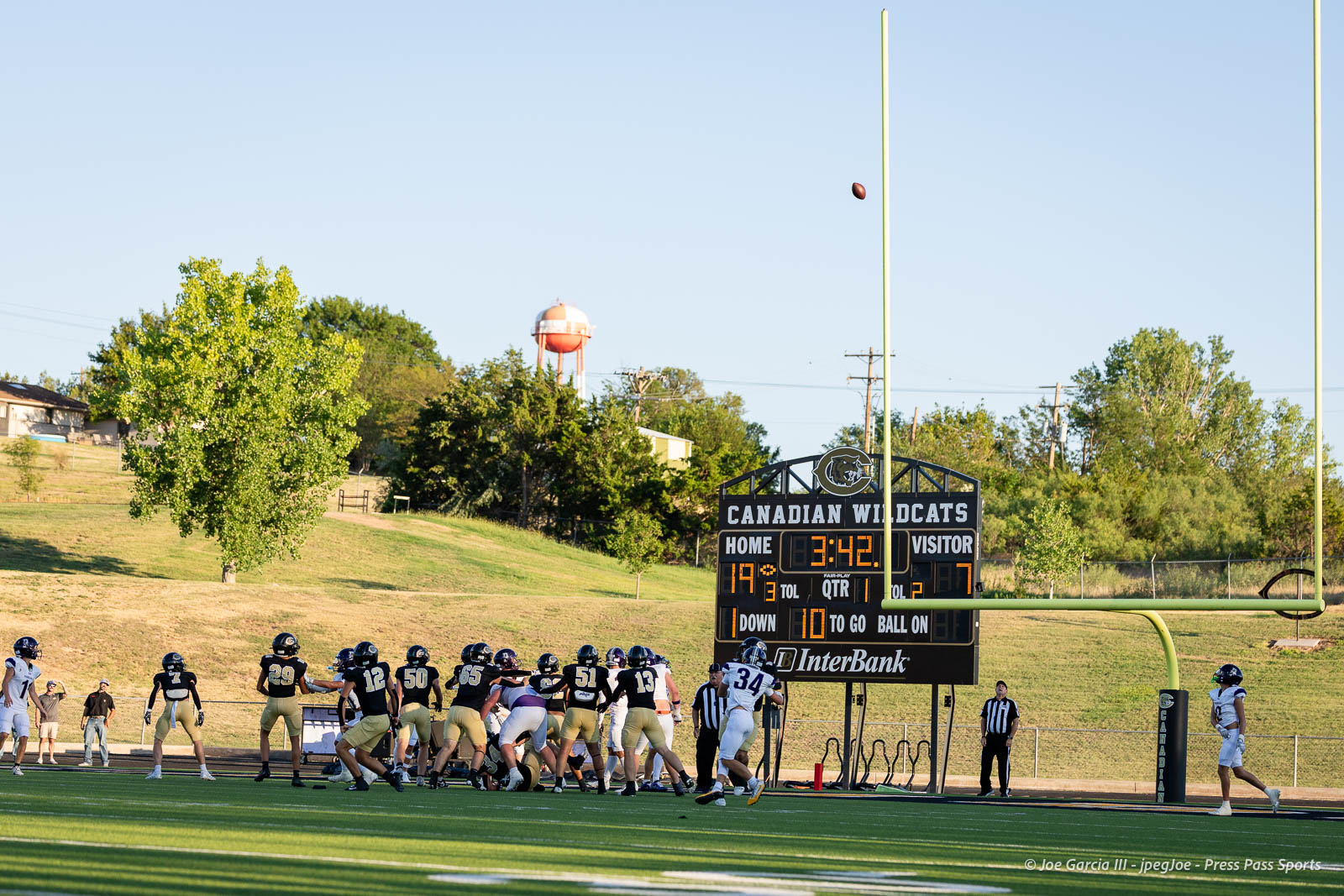 panhnandle-vs-canadian-football-jpegJoe-pps-7 | Press Pass Sports High school football teams line up at the line of scrimmage on a sunny field with a scoreboard reading Canadian Wildcats in the background.