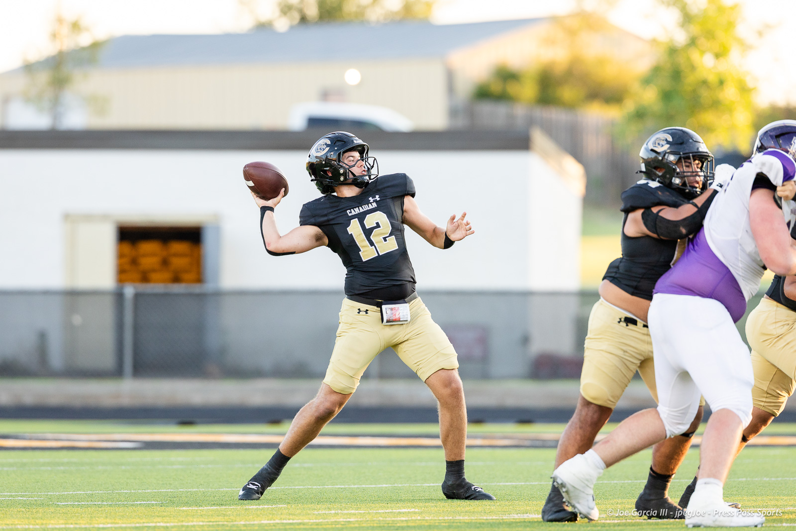 panhnandle-vs-canadian-football-jpegJoe-pps-9 | Press Pass Sports High school football quarterback in black jersey (number 12) throwing a pass during a play on a green field.