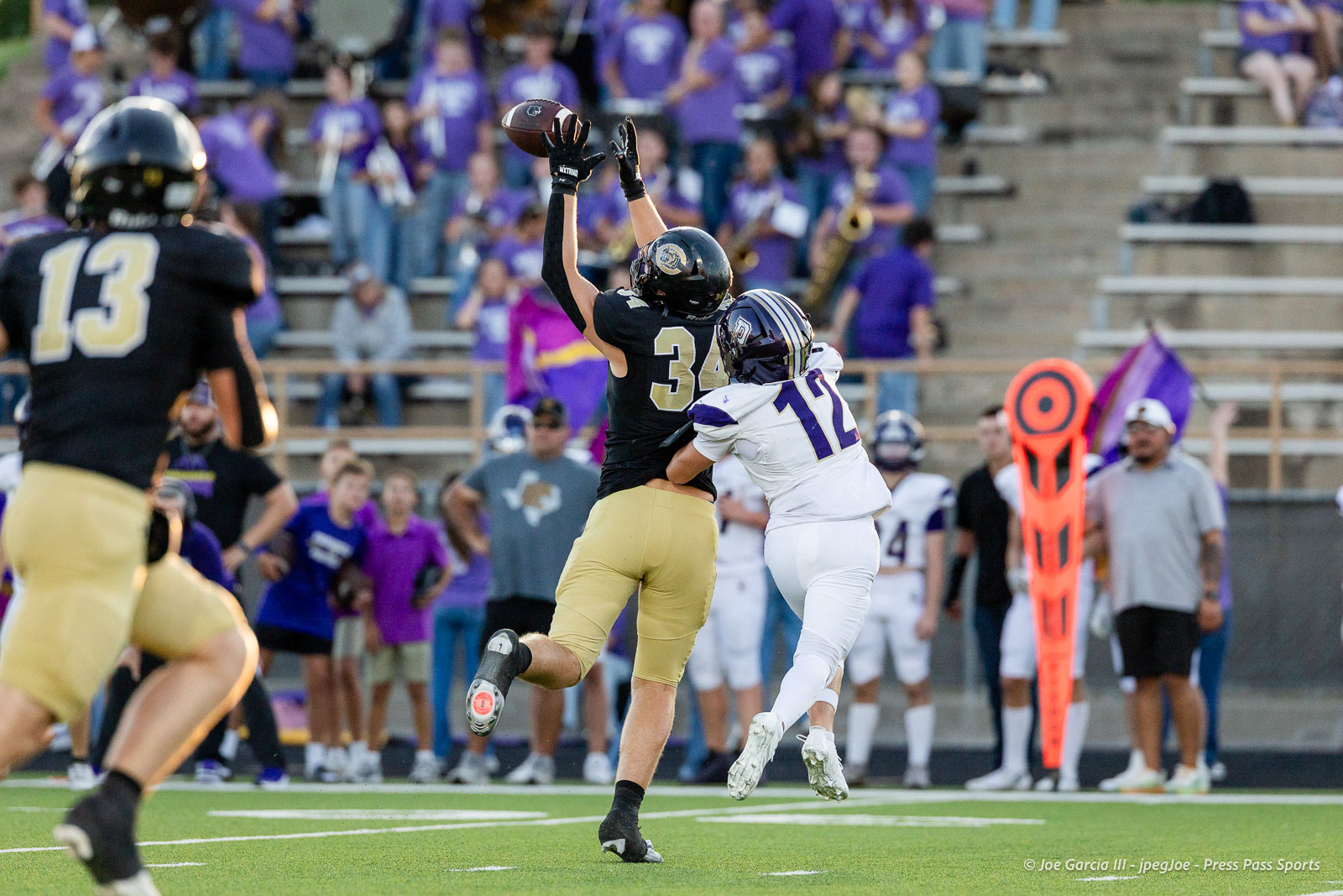 panhnandle-vs-canadian-football-jpegJoe-pps-11 | Press Pass Sports Players leap for a football near the sideline as fans in purple look on from the stands.