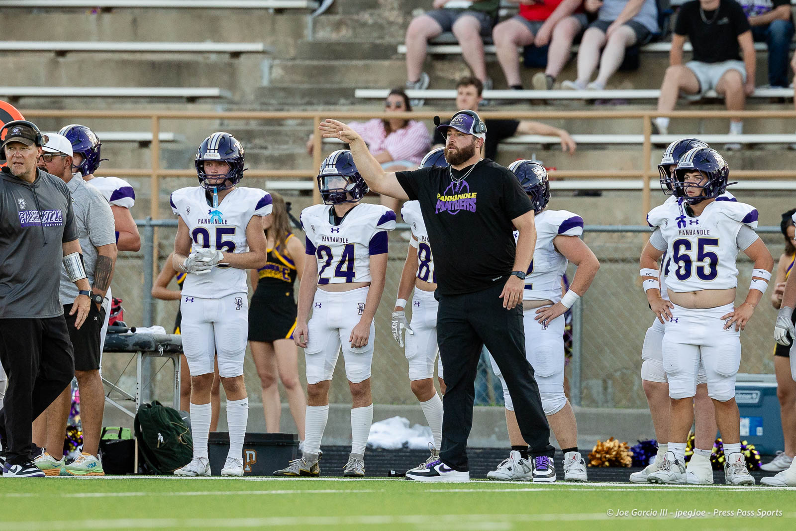 panhnandle-vs-canadian-football-jpegJoe-pps-12 | Press Pass Sports Panhandle Panthers football coach signals from the sideline while players in white and purple uniforms stand nearby on the sideline.