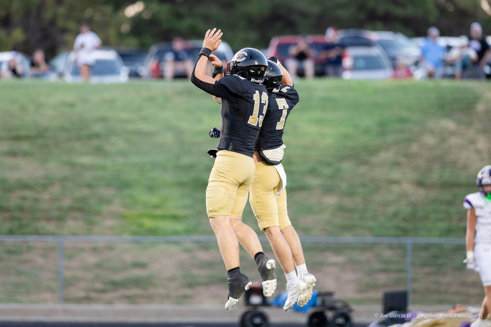 panhnandle-vs-canadian-football-jpegJoe-pps-14 | Press Pass Sports Two football players in black jerseys and gold pants jump in celebration on the field, raising their hands as spectators watch in the background.