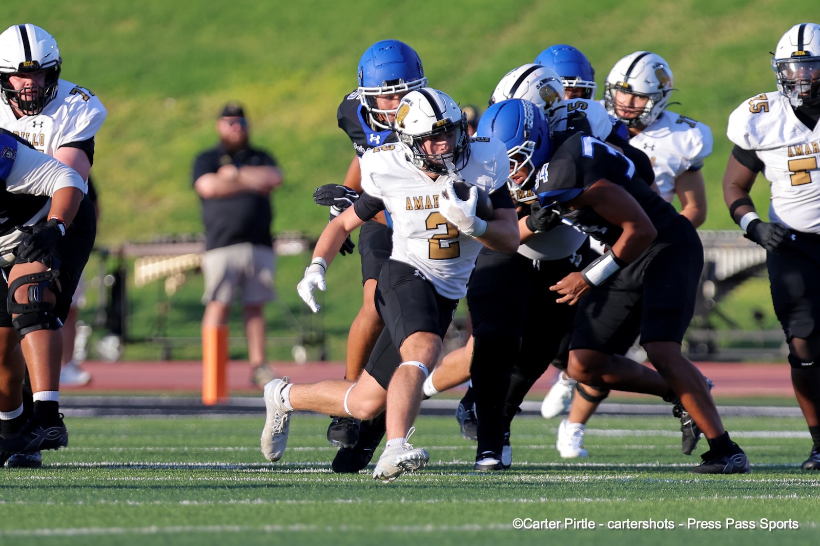 Running back wearing number 2 in a white jersey carries the ball as defenders close in during a football game on a sunny field.