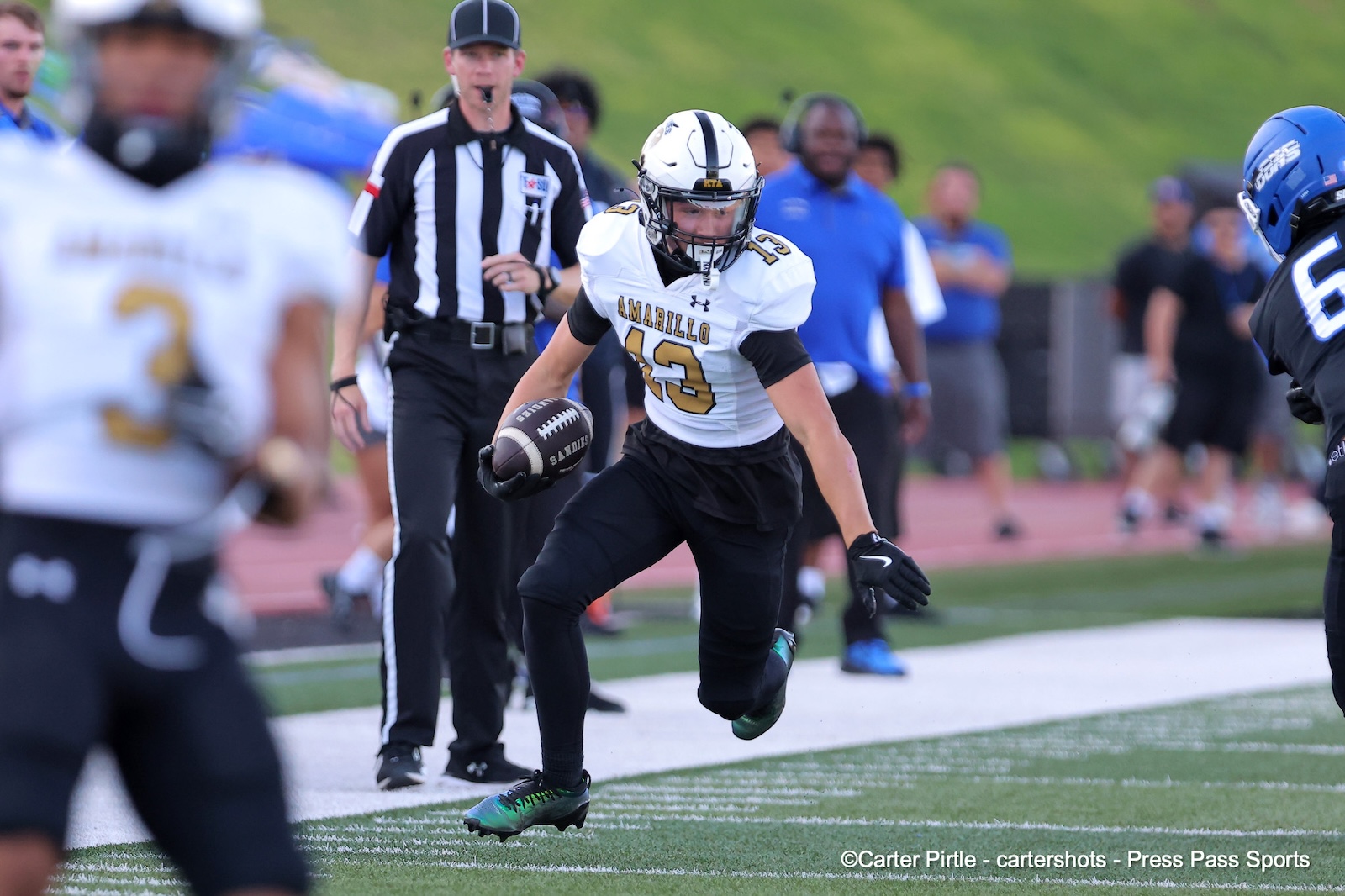 Football player in a white Amarillo jersey (number 43) runs with the ball during a game, with a referee and teammates in the background.