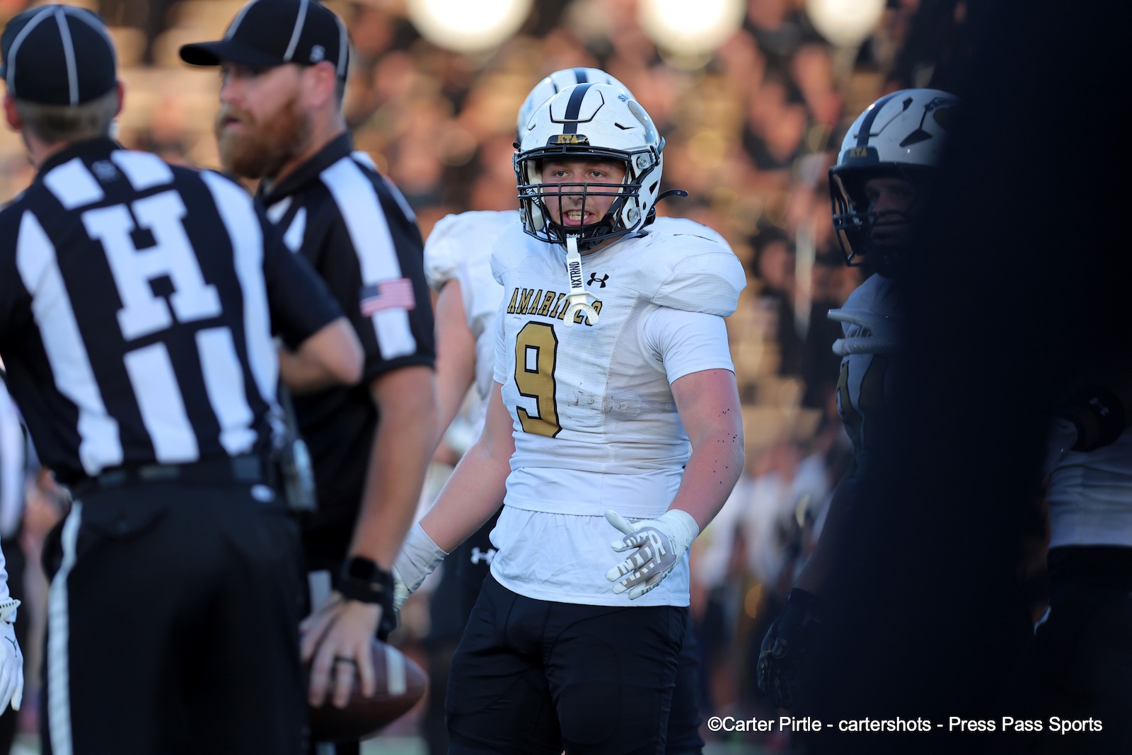 Football player in a white jersey with the number 9 and a helmet, standing on the field during a game with a referee nearby.