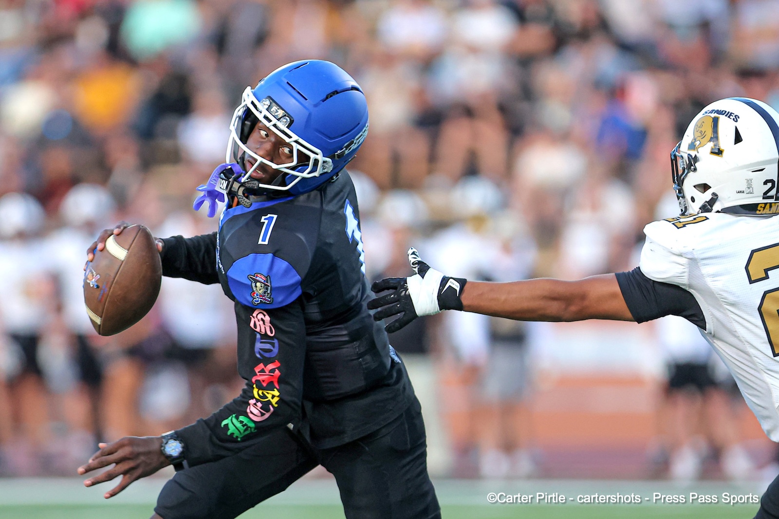 Football player in a blue helmet dodges a tackle while keeping the ball tucked under his arm on the field.
