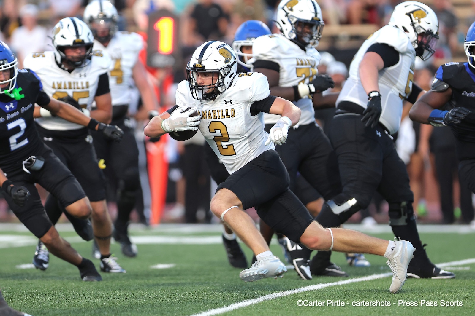Amarillo football player wearing number 2, carrying the ball and sprinting past defenders on a green field.